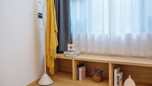 A room with a wooden bench, a white floor lamp, a yellow throw, a white vase, and books on the bench. - Homie Inn (Changsha)