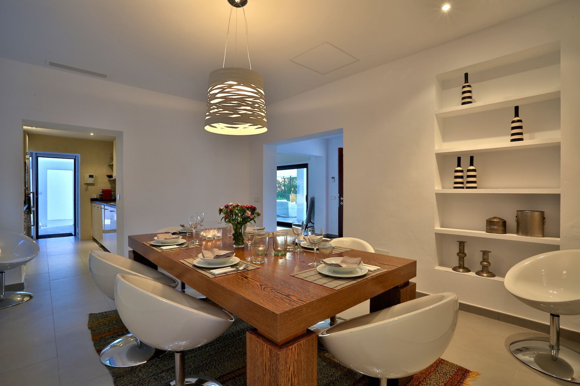 A modern dining area with a wooden table, white chairs, and a hanging light fixture.