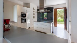 Une cuisine moderne avec des meubles blancs, une hotte en acier inoxydable et une machine à café rouge.
