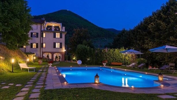 A swimming pool with a stone pathway leading to it, surrounded by lounge chairs and umbrellas.
