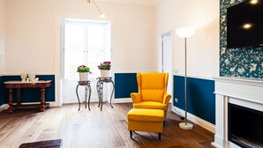 A room with a wooden floor, a yellow armchair, a small table with potted plants, a floor lamp, and a fireplace. - Interno Sorrentino with sea view - My Rental Homes (Sorrento)