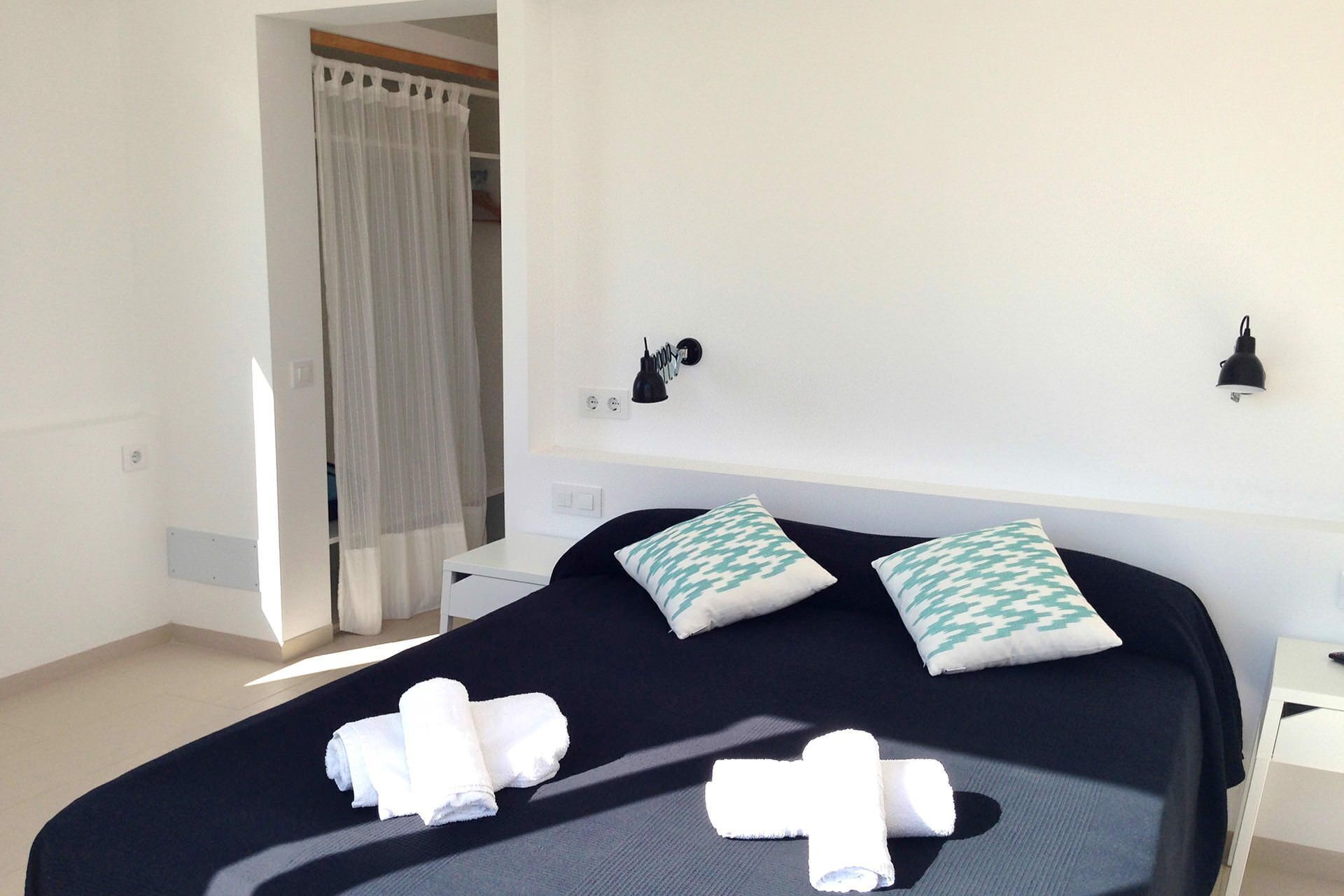 Een hotelkamer met een bed, twee kussens, een nachtkastje, een lamp en een gordijn.