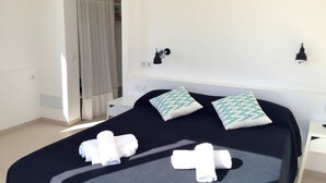 A hotel room with a bed, two pillows, a nightstand, a lamp, and a curtain. - My Rental Homes - Nure Villa 2 with private pool, air conditioning and wifi (Ciutadella)