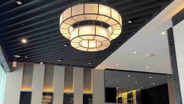 Un hall d’entrée moderne doté d’un grand lustre circulaire, d’un espace salon avec des canapés et des tables, et d’un plafond haut avec des poutres apparentes.