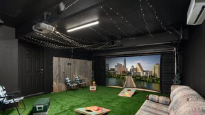Een kamer met kunstgras, een beamer, een scherm, een bank en uitzicht op een stadslandschap.