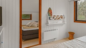 Une chambre à coucher comprenant un lit, une commode, un miroir, une étagère avec des objets décoratifs et une fenêtre donnant sur des arbres.