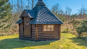 Une petite cabane en rondins, dotée d’un toit à forte pente, d’une cheminée et d’une porte avec une fenêtre.