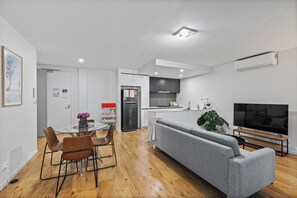 Un salon moderne avec un canapé gris, un téléviseur et un coin repas comprenant des chaises et une table.