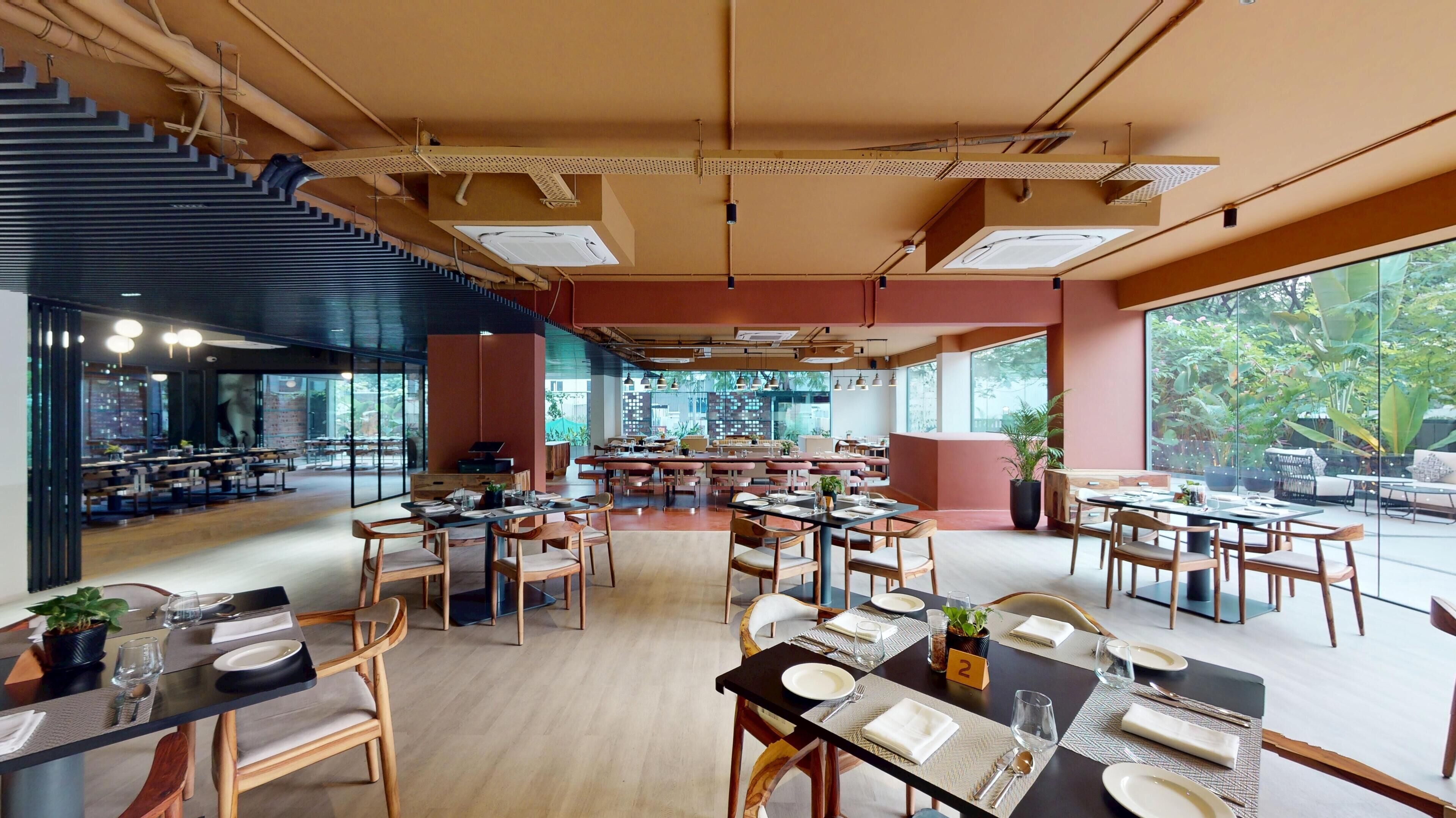 A spacious restaurant with multiple dining areas, large windows, and a staircase leading to an upper level.