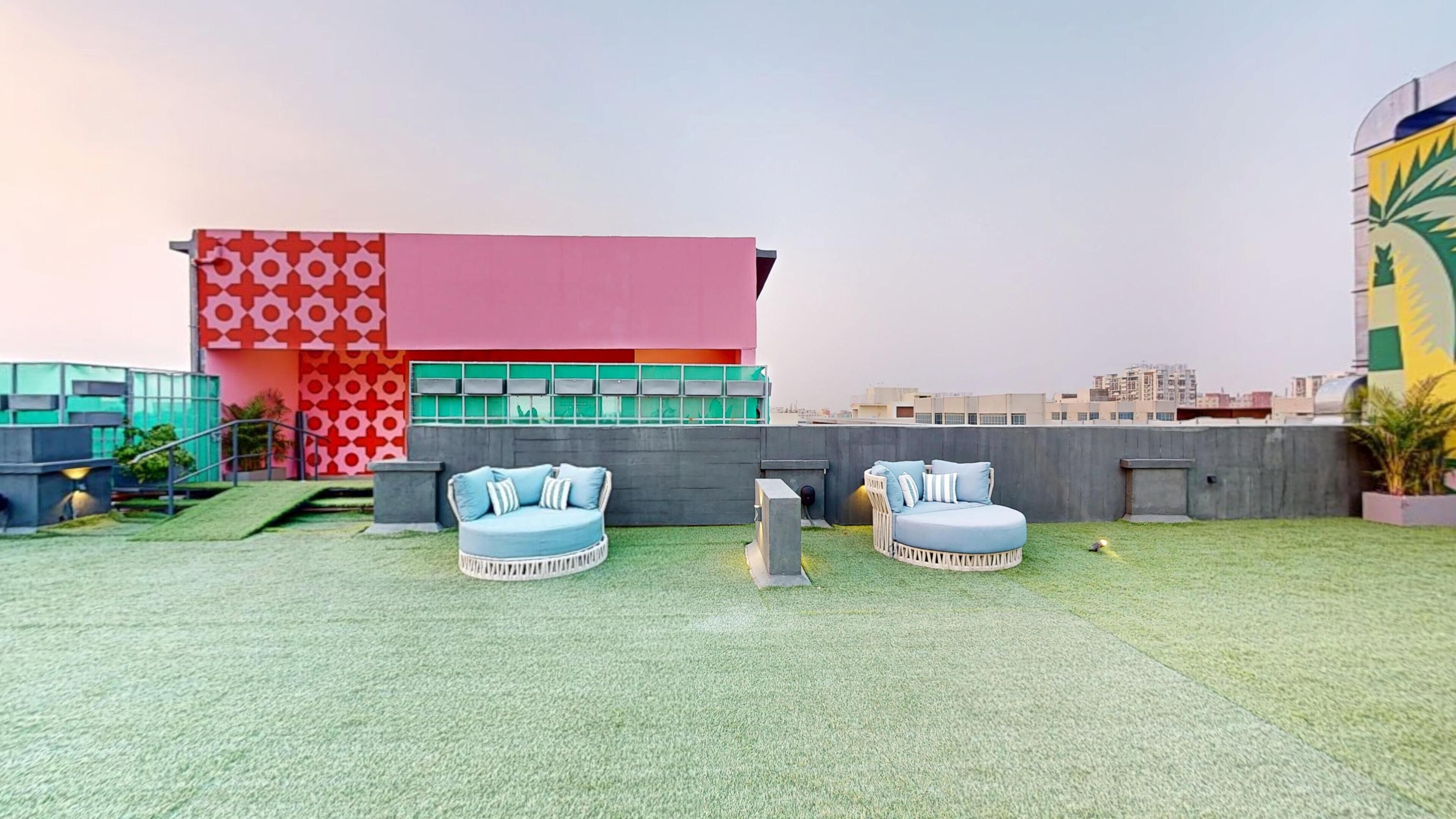 Une terrasse sur le toit avec deux espaces de détente circulaires et, en arrière-plan, un bâtiment moderne à la façade rouge et rose.