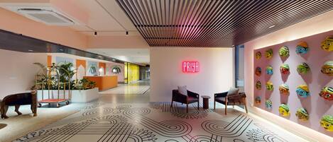 A modern hotel lobby with a reception desk, seating area, decorative wall art, and a patterned floor.