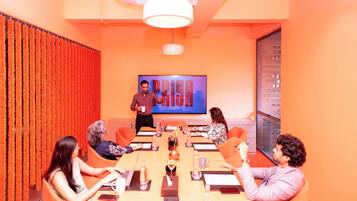 A conference room with a large screen displaying the word "PRYA" and a man presenting.