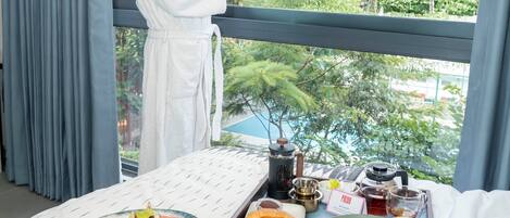 A hotel room with a balcony, a breakfast tray with various foods, and a view of greenery outside.