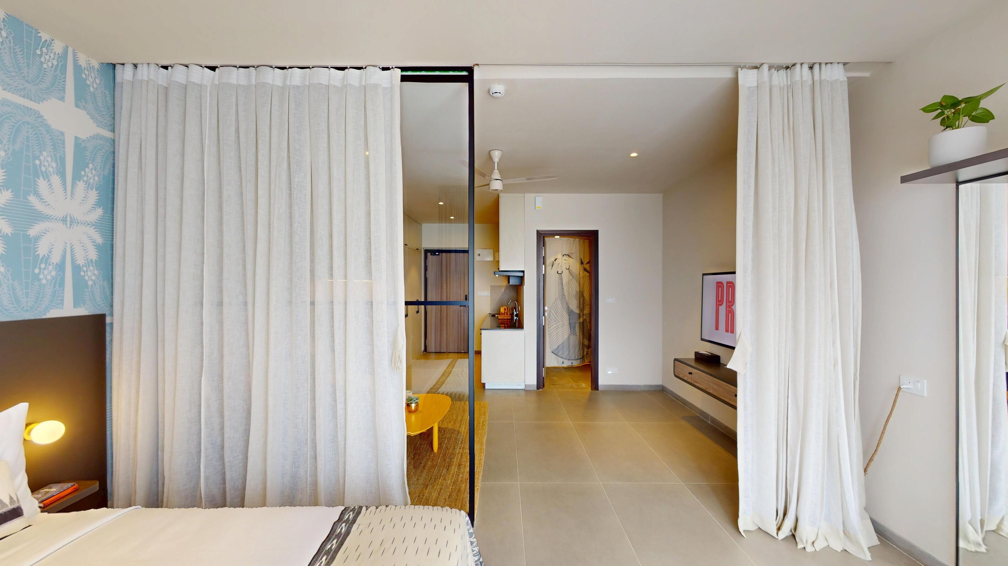 Habitación de hotel moderna con cama, escritorio, televisión y vista al pasillo.