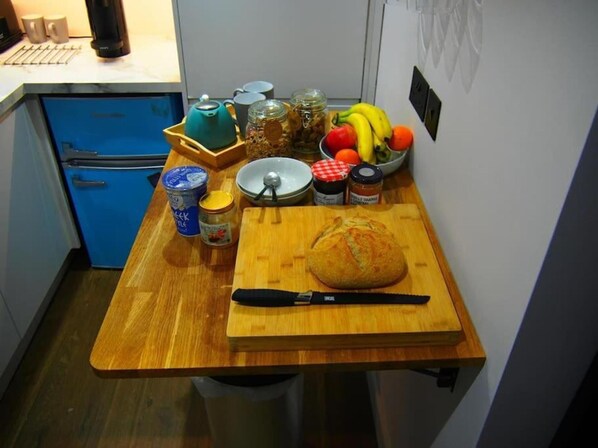 A kitchen counter with a loaf of bread, a knife, jars of preserves, a teapot, and a bowl of fruit. - Central 2B Sleep3 Gem-zen Courtyard, Late Checkout (Frome)