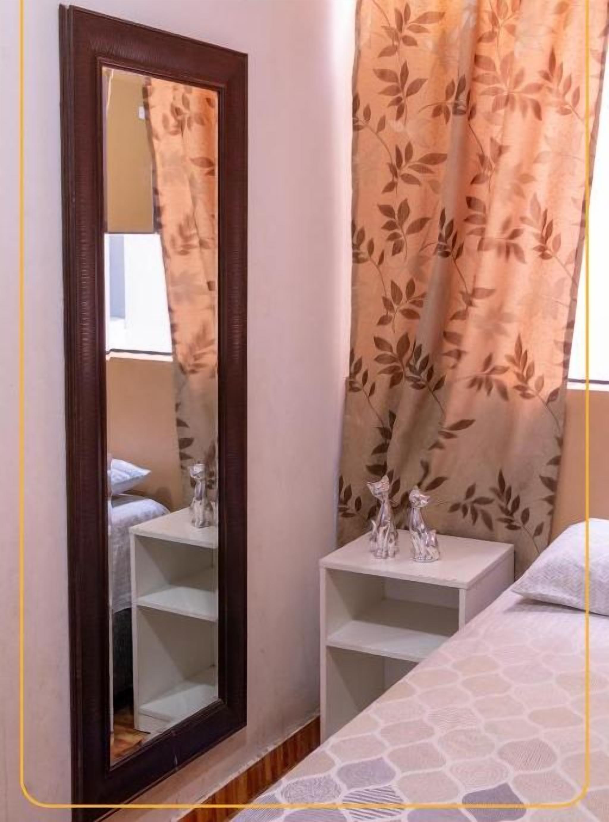 Quarto com cama, mesa de cabeceira, espelho e janela com cortinas.