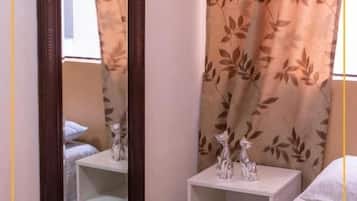 Quarto com cama, mesa de cabeceira, espelho e janela com cortinas.