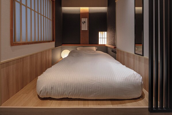 A neatly arranged room with a bed, a wall-mounted shelf, and a window with vertical blinds. - ENSO TOKYO AKASAKA - Hostel (Tokyo)