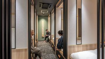A hotel corridor with a narrow walkway, wooden paneling, and a bed on the right.