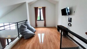 Una habitación con techo inclinado, una ventana con cortinas, un televisor montado en la pared y una cama con barandilla de metal.