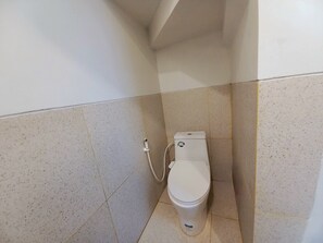 A small, white toilet with a bidet attachment in a tiled bathroom. - Homestay Jogja Simply Homy Unit Jambon (Sleman)