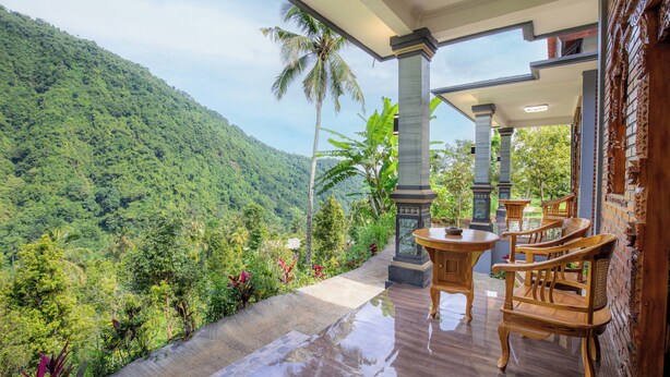 Une terrasse offrant une vue sur une végétation luxuriante et une montagne. On y trouve des chaises et une table en bois.