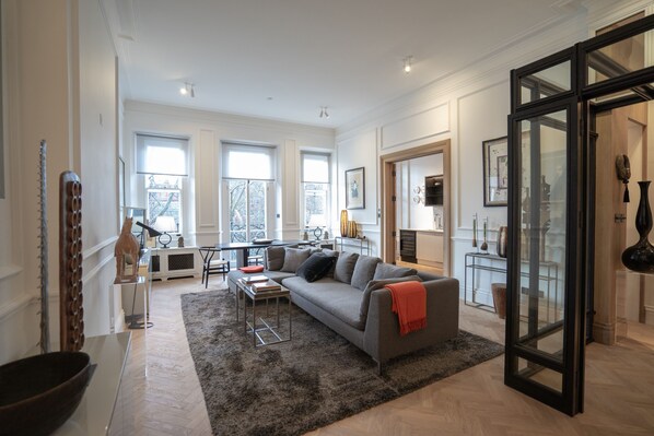 A spacious living room with a gray sofa, a coffee table, and a large window.