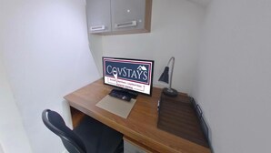 Ein kleiner Arbeitsraum mit Schreibtisch, Computermonitor, Tastatur, Stuhl, Lampe und Schrank.