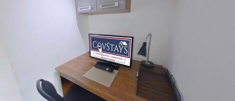 Un pequeño espacio de oficina con un escritorio, un monitor de computadora, teclado, una silla, una lámpara y un armario.