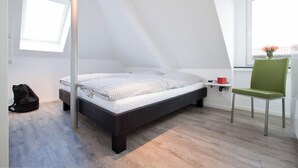 Un dormitorio moderno con techo inclinado, una cama, un sillón y una ventana.
