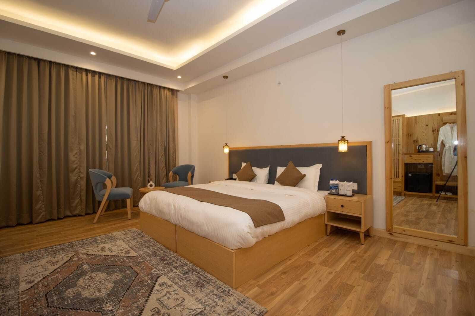 A modern hotel room with a large bed, two chairs, a nightstand, a mirror, and a wooden floor.