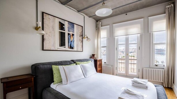 A bedroom with a large bed, a nightstand, a dresser, and a view of the city through large windows. - Balat 5 (Fatih)