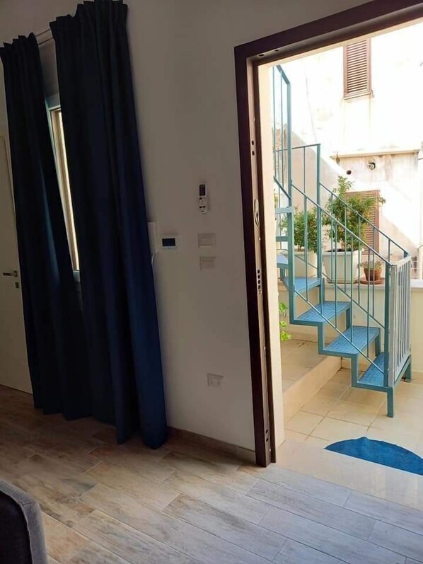 A room with a wooden floor, a dark curtain, a door, and a view of a blue staircase leading to an outdoor area with potted plants. - La Grazia Trani (Trani)