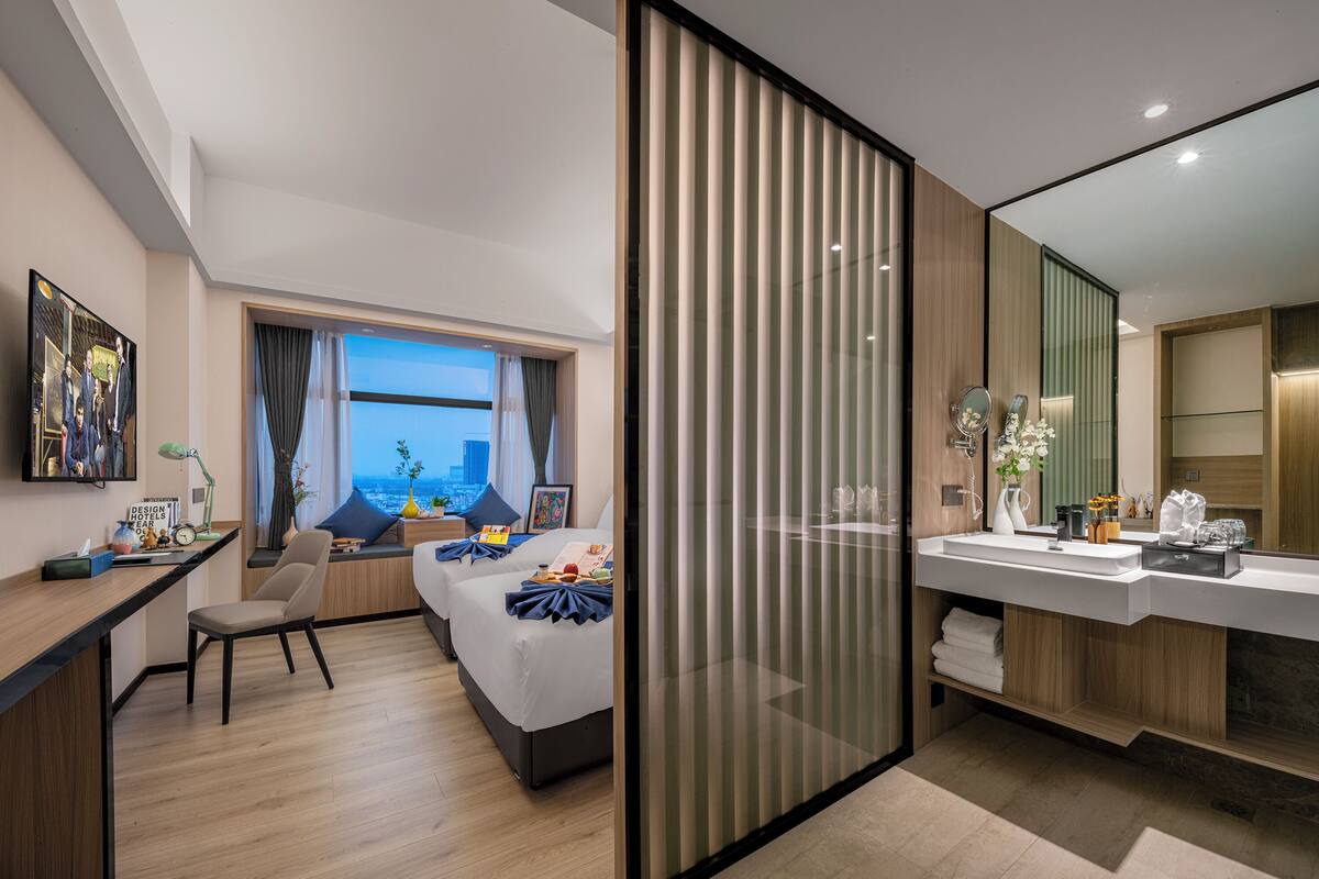 A modern hotel room with a bed, desk, and a large window offering a city view.