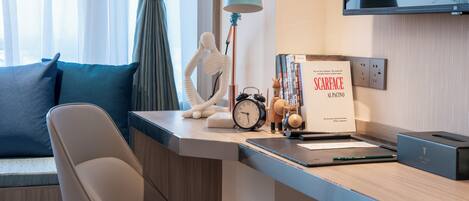A modern hotel room with a desk, a chair, a lamp, a clock, a decorative figure, and a book titled "SCARFACE AL PACINO".