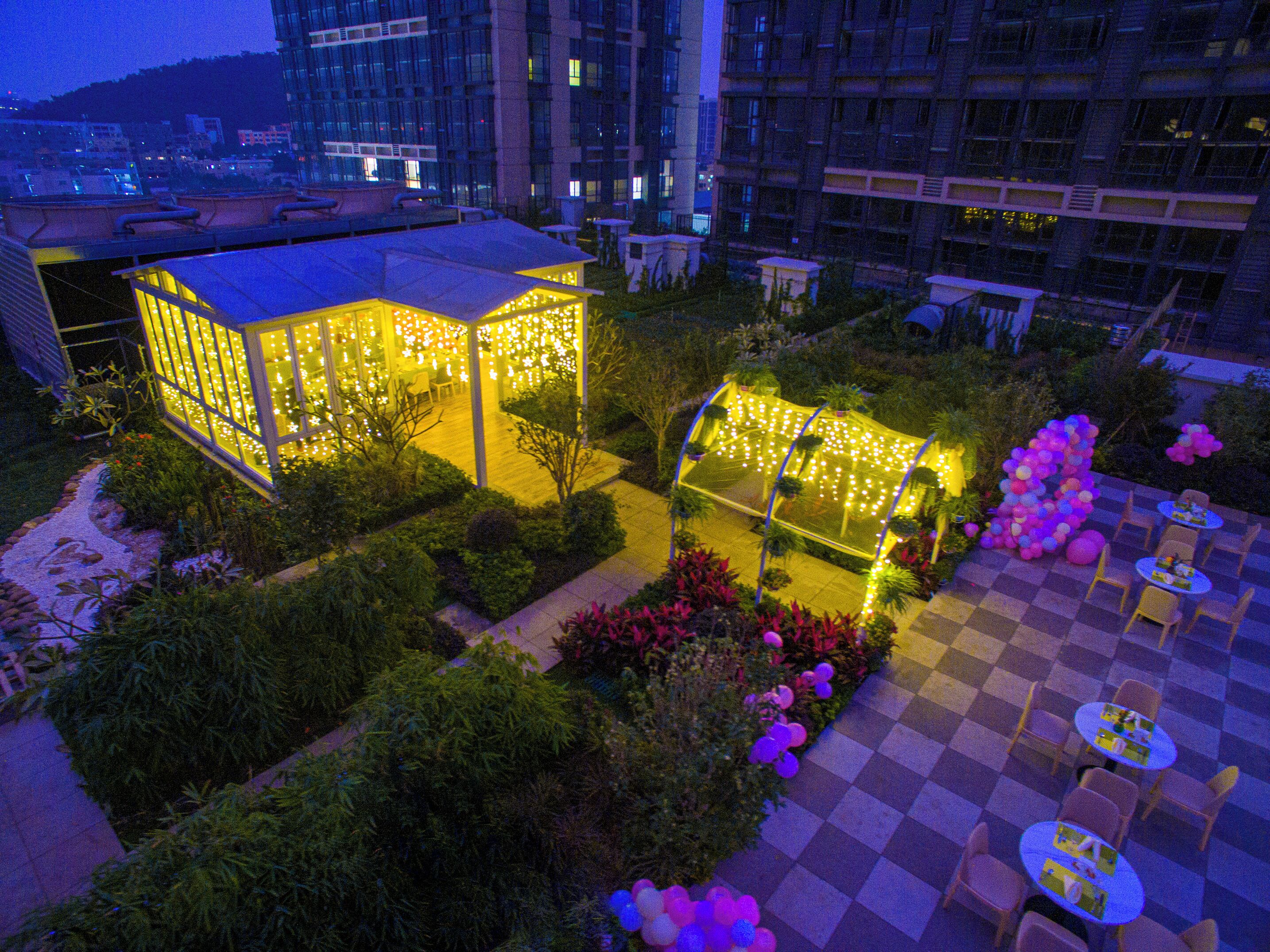 Un jardín en la azotea con zonas de estar, estructuras iluminadas y suelo a cuadros.