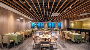Een ruime eethoek met meerdere tafels en stoelen, houten balken in het plafond en grote ramen met uitzicht op de stad.