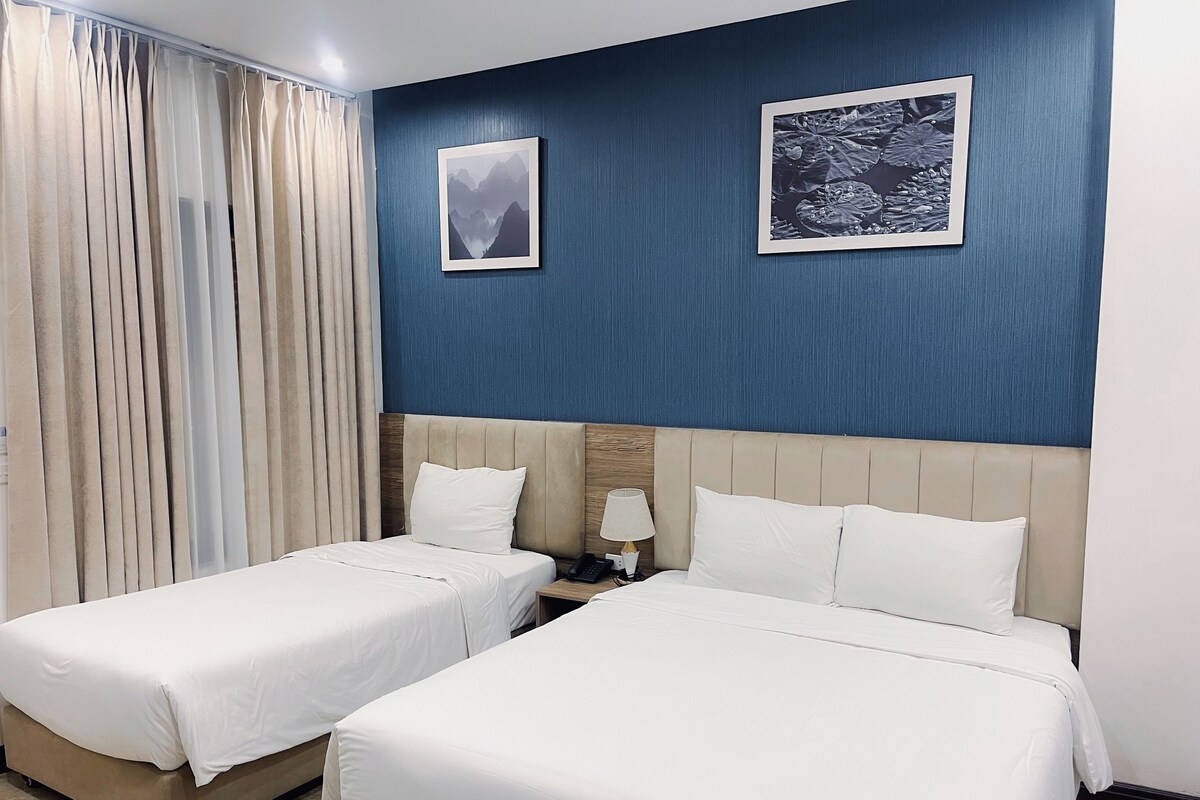 Une chambre d’hôtel avec deux lits, une table de chevet, une lampe et deux tableaux encadrés au mur.