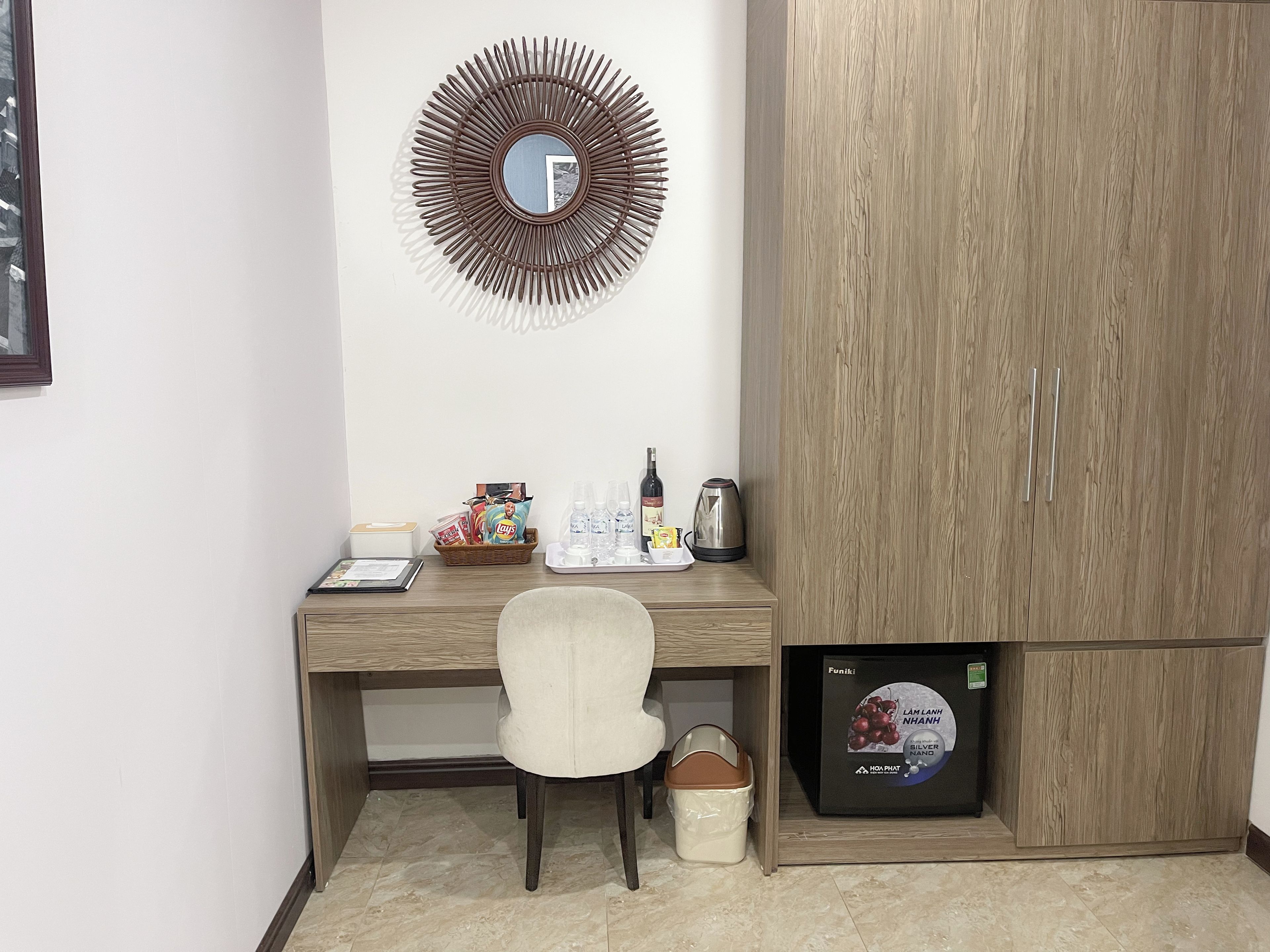 Una habitación con un escritorio de madera, una silla, un espejo, un armario y un refrigerador.
