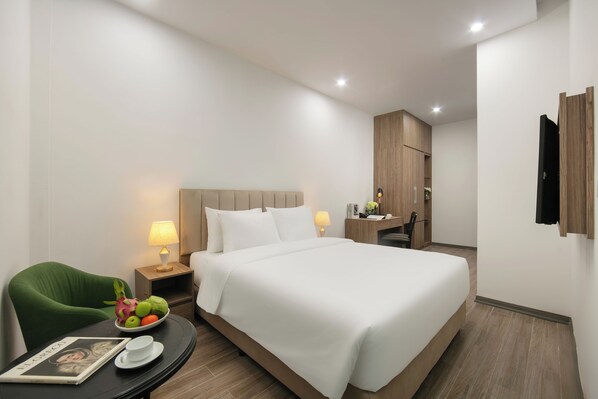Ein Hotelzimmer mit einem großen Bett, einem grünen Sessel, einem Nachttisch mit Lampe, einer Obstschale und einer Zeitschrift.