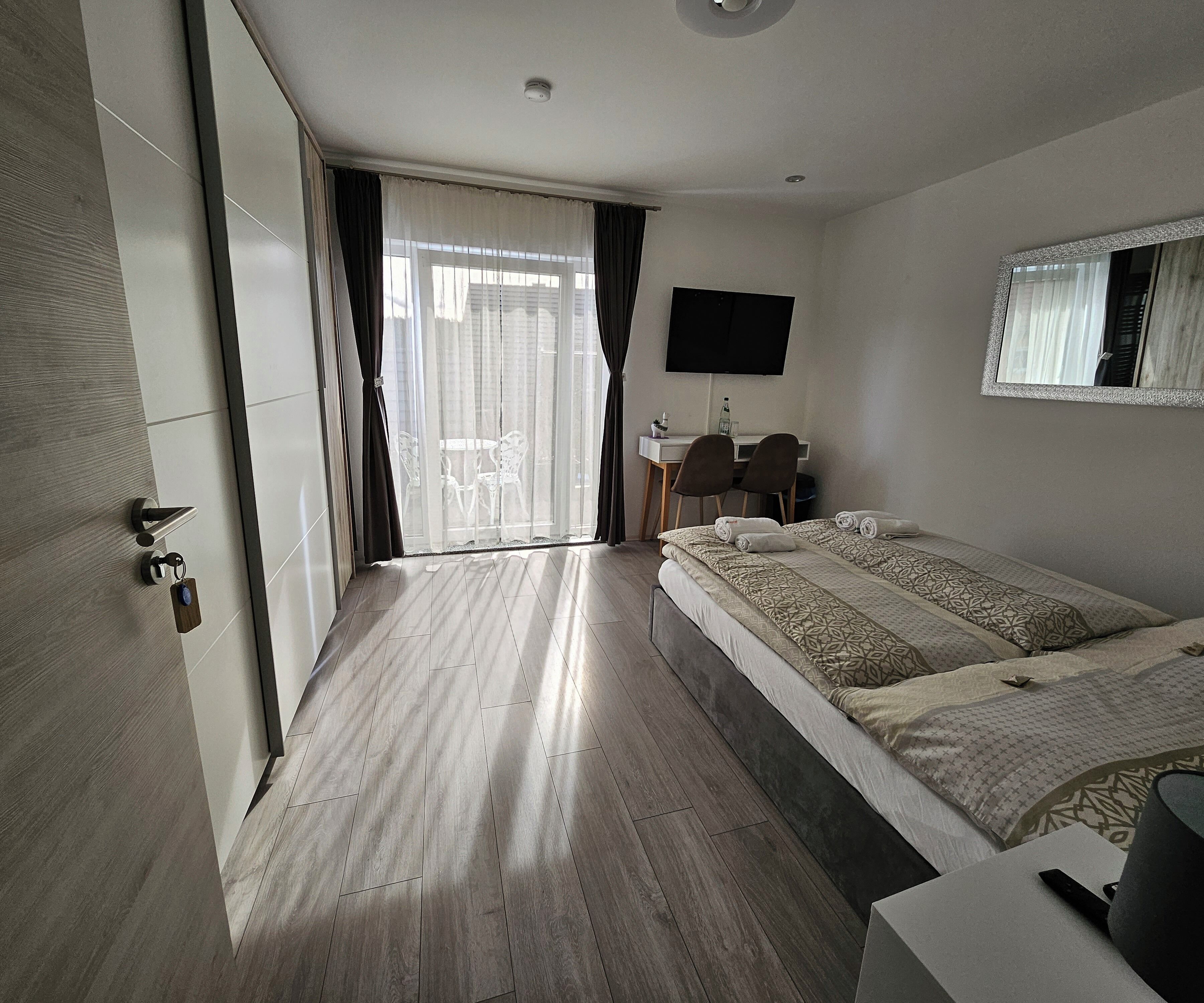 Camera d'albergo moderna con un ampio letto, una scrivania con sedie, una televisione a schermo piatto e una porta-vetro scorrevole che dà su un balcone.