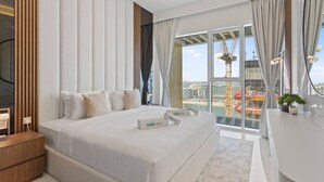 A modern hotel room with a large bed, a desk, and a view of a cityscape. - Coastal Elegance 1-Bedroom in Grand Bleu (Emaar Beachfront)