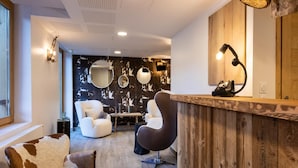 A modern interior with a wooden reception desk, two chairs, a round mirror, and a wall with a distressed pattern.