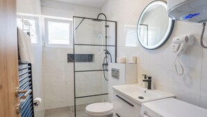 Moderni kylpyhuone, jossa on lasinen suihkuseinä, wc, peilillä varustettu pesuallas ja seinälle asennettu hiustenkuivaaja.