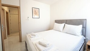 Hotellihuone, jossa on sänky, valkoiset vuodevaatteet, seinällä oleva kehystetty kuva ja puinen ovi.