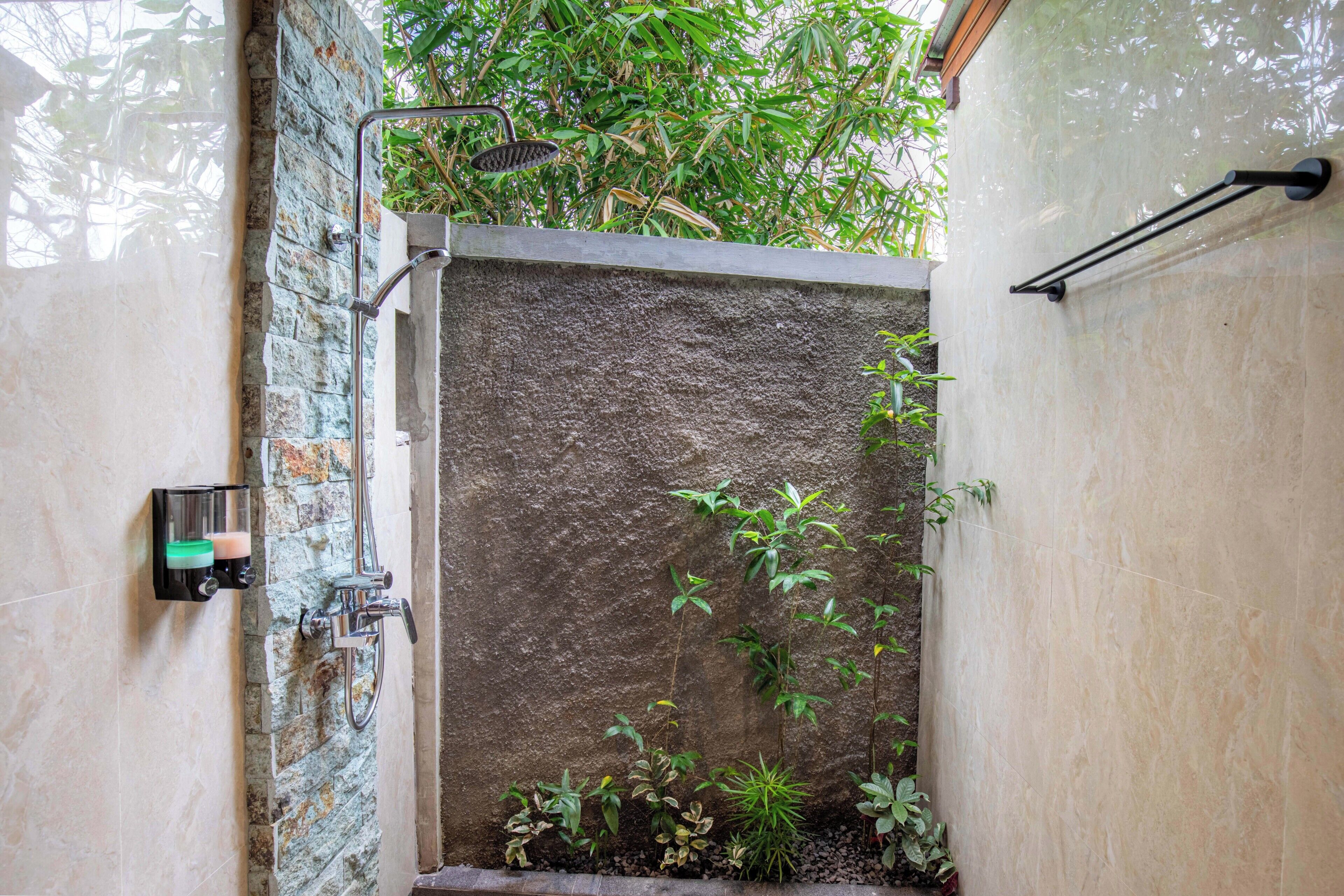 A shower area with a stone wall, a handheld showerhead, and a soap dispenser.