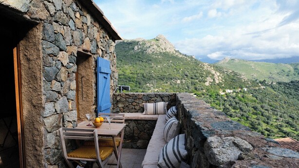 A stone building with a wooden table and chairs, a blue door, and a stone bench with cushions. - Double room with terrace in a village house in Corbara (Corbara)