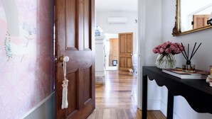A hallway with a wooden door, a clear chair, a black console table with a vase of flowers, and a mirror.