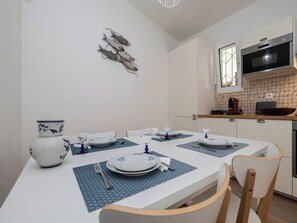 Un coin repas avec une table blanche dressée pour quatre personnes, des sets de table bleus et une décoration murale représentant un poisson.
