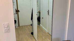 Un pasillo estrecho con suelo de madera, una puerta con manija metálica y un espejo que refleja parte del cuarto.